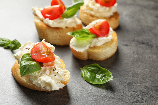 Pieces of baguette with tasty cream cheese and tomatoes on gray table