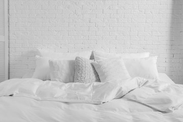 Large comfortable bed with pillows and blanket near white brick wall indoors. Stylish interior