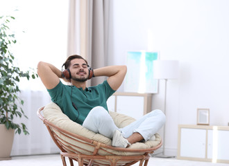 Handsome young man listening music in armchair at home. Space for text