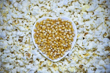 Corn kernels in the bowl of shape of heart with ready made popcorn around it.