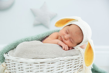 Adorable newborn child wearing bunny ears hat in baby nest indoors