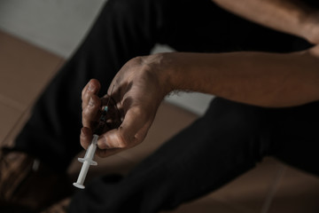 Young drug addict with syringe sitting on floor, closeup