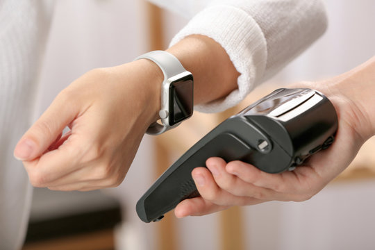 Woman using terminal for contactless payment with smart watch indoors