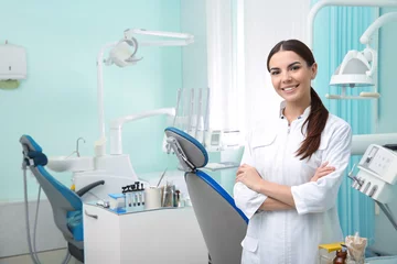 Foto op Plexiglas Tandarts Jonge vrouwelijke tandarts in witte jas op de werkplek. Ruimte voor tekst