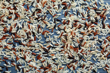Brown and other types of rice scattered on color wooden background