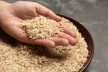 Foto op Canvas Woman holding grains near plate with brown rice on table, closeup © New Africa