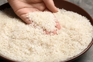  Woman holding grains near plate with rice on table, closeup © New Africa