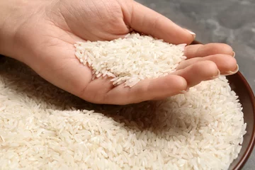 Gordijnen Woman holding grains near plate with rice on table, closeup © New Africa