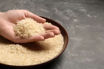Gordijnen Woman holding grains near plate with parboiled rice on table, space for text © New Africa