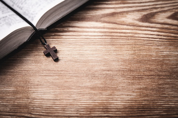 Holy Bible with wooden cross on wooden table.