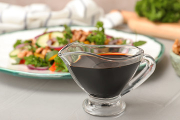 Balsamic vinegar in gravy boat near plate with salad on table