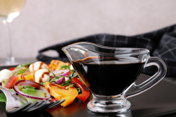 Gravy boat of balsamic vinegar on plate with vegetable salad, closeup