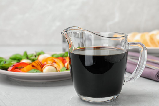Balsamic vinegar in glass jug near plate with salad on table