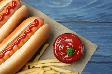Poster Composition with hot dogs, french fries and sauce on color wooden table, top view © New Africa