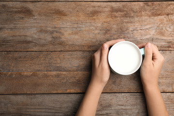 Woman holding cup of milk on wooden table, top view. Space for text