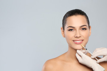 Young woman getting lips injection on grey background, space for text. Cosmetic surgery