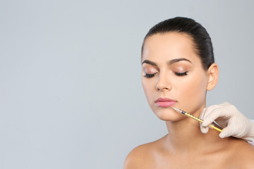 Young woman getting lips injection on grey background, space for text. Cosmetic surgery