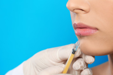 Young woman getting lips injection on color background, space for text. Cosmetic surgery