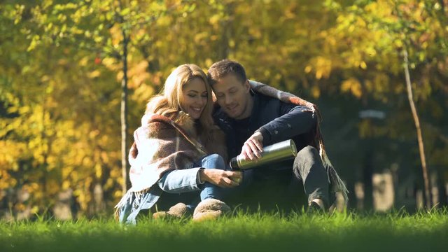 Couple in love covered with plaid drinking hot tea from thermos, having fun