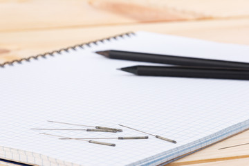 Silver needles for traditional Chinese medicine acupuncture lie on a note book, on a wooden table.