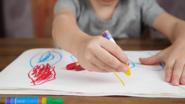 A child of preschool age holds a bright pencil and draws on white paper close-up. The concept of education and development of children.
