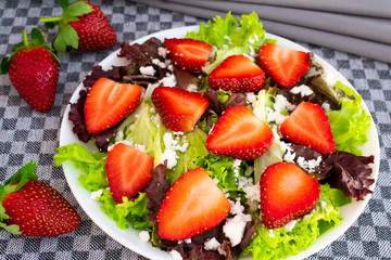 Vegetarian delicious fresh salad with purple and green lettuce leaves, strawberries and goat cheese on grey tablecloth.