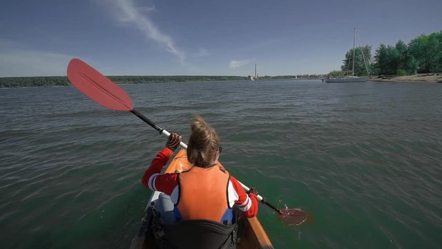 A young girl in a life jacket and glasses rowing on a kayak by the sea with a dog Beagle. Around the beautiful nature, blue water. Rear view.