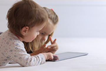 Two baby girls lying on bed with a tablet, close-up view