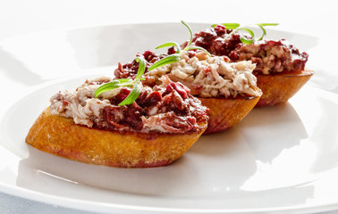 rabbit rillettes toppled with cranberry red wine confiture spreaded over fired white bread slices and decorated with rosemary