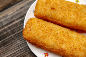 Crispy breaded fried hake fish fillet on old wooden table