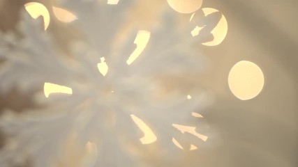 A white artificial snowflake decorated with shiny powder on a leafless tree, close-up. Plastic christmas tree toy and bokeh effect on warm multicolor background. Christmas party decoration.