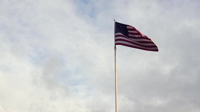 American flag flying in the wind at sunrise with blue sky and clouds. slow motion footage in 1080p