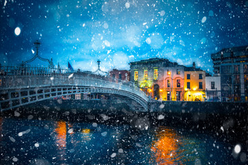Fototapeta premium Wieczorny widok na Dublin Irlandia na most Ha'Penny na rzece Liffey z płatkami śniegu spadającymi podczas zimowej burzy śnieżnej