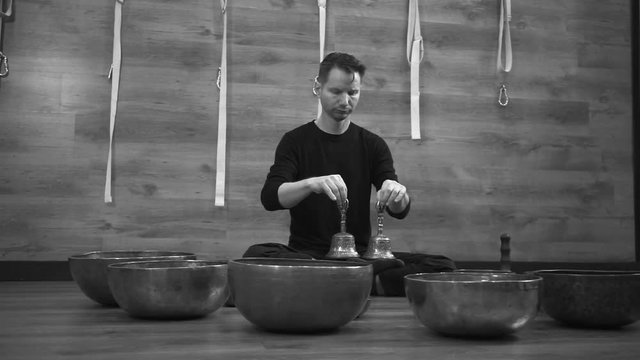 Man sits near Tibetan singing bowls with bells in their hands
