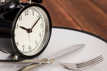 Alarm clock on plate with knife and fork on wooden background. Time to eat. Weight loss or diet concept