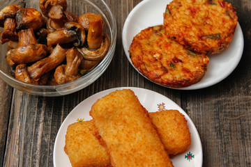 Crispy breaded fried fish fillet, vegetarian burger made from various type of vegetables and grilled champignons mushroom on old wooden table