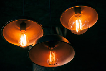 Three orange decorative lamps in the darkness hanging in the ceiling, close up