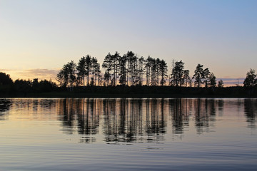 Fototapeta premium Silhouettes of trees and colorful sky are reflected in the forest lake in the evening. Unusual and picturesque scene. Russia.