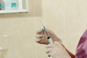 The doctor's hands in medical gloves hold a medicine-filled insulin syringe in the manipulation...