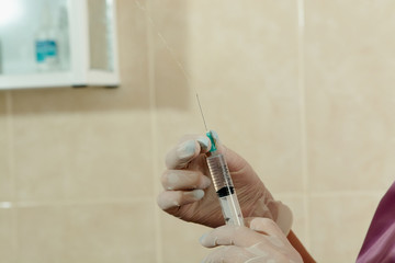 The doctor's hands in medical gloves hold a medicine-filled insulin syringe in the manipulation...
