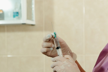 The doctor's hands in medical gloves hold a medicine-filled insulin syringe in the manipulation...