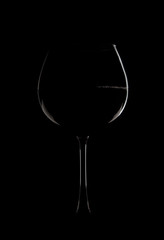 Photo of a glass with wine on a black background. The edges of the glass are illuminated with light.