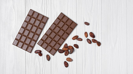 Top view on tasty chocolate bars and cocoa beans on white wooden background