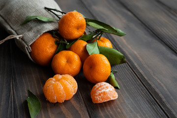 The atmosphere of Christmas and New Year: Fresh tangerine with green leaves on a dark wooden background. Mandarin peeled and disassembled into slices, cinnamon sticks, cones, tangerine peels, leaves.