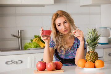 Pretty woman drinking juice on kitchen, fruits on a table, healthy lifestyle