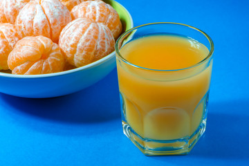 Tangerines in a plate, a glass of tangerine juice on a blue background. Close-up