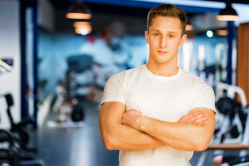 Fototapeta na wymiar Young handsome fitness trainer sits modern gym