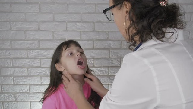 Doctor checks the tonsils of kid. The pediatrician examines the throat of a little girl.