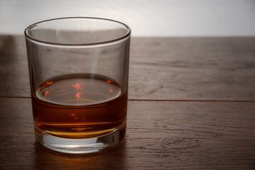 A glass of whiskey stands on a wooden table in backlight