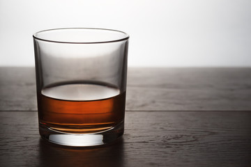 A glass of whiskey stands on a wooden table in backlight